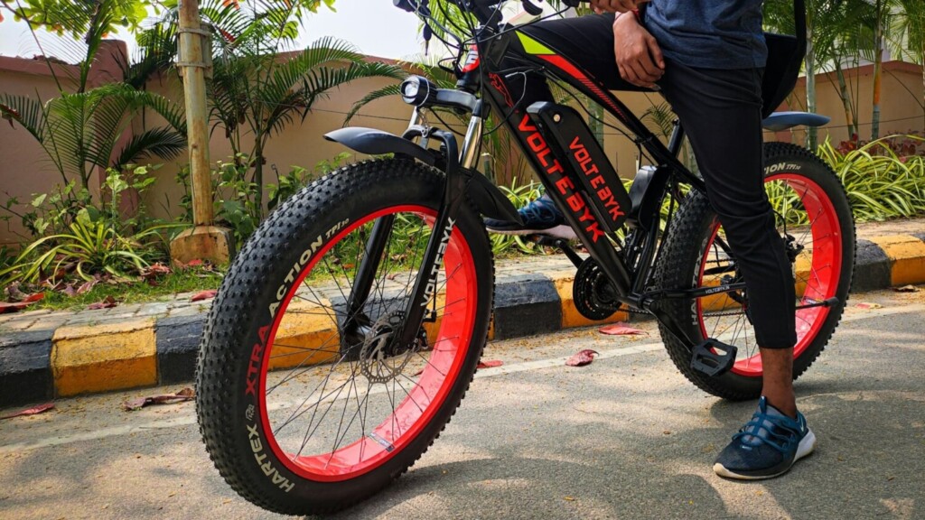 Elektrische fatbike met rode velgen op straat, gebruikt door een jongere in stedelijke omgeving.